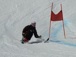 Young woman Maddie Watts sit-skiiing down a mountain.