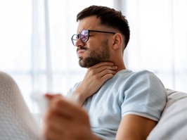 Sick man lying on the couch with high temperature and holding his throat with hand.