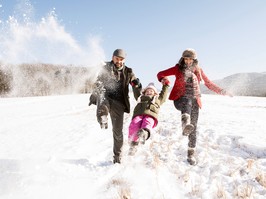 Father and mother having fun with their daughter, playing in the snow. Sunny white winter nature.