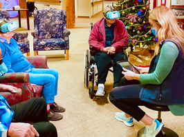 Group of seniors wearing virtual reality headsets while facility staff watches on a tablet