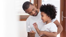Happy African American Family, Dad teaching his son in white shirts brushing teeth in bathroom together. Father and kid boy in curly hair enjoying with dental hygiene at home in morning