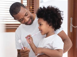 Happy African American Family, Dad teaching his son in white shirts brushing teeth in bathroom together. Father and kid boy in curly hair enjoying with dental hygiene at home in morning