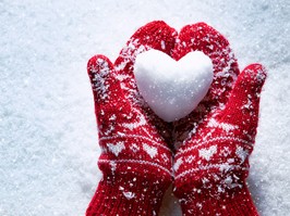 Female hands in knitted mittens with snowy heart against snow background. Love, winter and Valentines day romantic creative concept with copy space for text