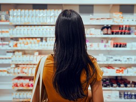 Young woman standing against shelf in pharmacy searching for medicine