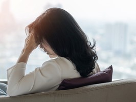 Women sitting on a couch holding her head in distress. Photograph from behind.