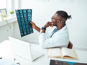 Young doctor looking at computed tomography x-ray image. Confident pleasant doctor working with MRI scan results. Radiologist man checking x-ray, health care, medical and radiology concept