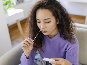 Asian woman using cotton swab while doing coronavirus PCR test. Woman takes coronavirus sample from her nose at home. woman at home using a nasal swab for COVID-19. - stock photo