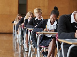 Teenage Students In Uniform Sitting Examination In School Hall