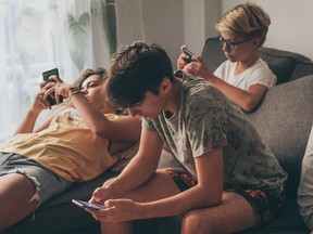 Group of teenager using smartphone sitting on a sofa at home. Young boys and a girl sharing photo and video watching social story online. Friends enjoying new trend technology. Youth and tech concept