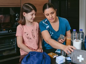Mother preparing emergency backpack with her daughter in the kitchen