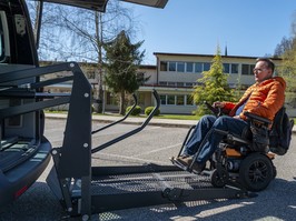 Disabled man in a motorized wheelchair when entering a van on an electric lift. In front of the vehicle, on the vehicle.