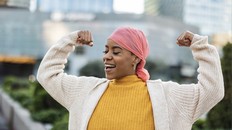 Latina woman, fighting breast cancer, wears a pink scarf, and clenches her arms as a survivor fighter