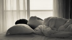 Young woman lying in bed, looking towards through the window - black and white photo.