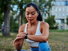 Female athlete setting up smart watch before workout in a forest. Beautiful asian sportswoman checking data on her gadget outdoor.
