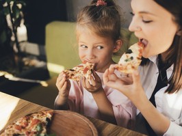 Happy mother and daughter eat pizza in a cafe and having fun.