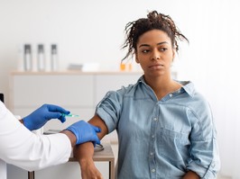 Vaccination Concept. Portrait Of Young Black Lady Receiving Vaccine Injection In Arm Sitting With Doctor In Hospital. Flu And Corona Virus Population Immunization, Cure Medicine And Treatment