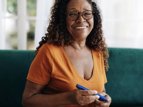 Black woman with diabetes uses a smart insulin pen to monitor and control her blood sugar levels, automatically recording the dose of insulin administered which helps manage the health condition.