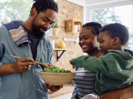 Happy African American man and his family preparing salad in the kitchen.