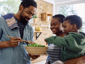 Happy African American man and his family preparing salad in the kitchen.