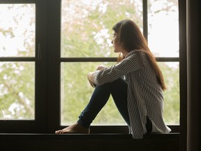 Thoughtful girl sitting on sill embracing knees looking at window, sad depressed teenager spending time alone at home, young upset pensive woman feeling lonely or frustrated thinking about problems
