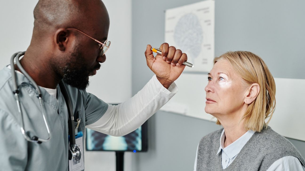 Male opthalmologist in uniform examining retina of mature female patient with astigmatism with help of medical device