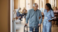 Happy senior man using mobility walker while African American nurse is helping him in nursing home.