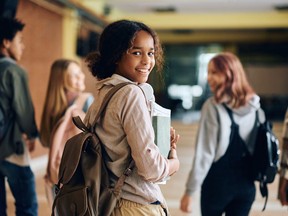 Happy African American high school student walking through hallway with her friends and looking at camera.