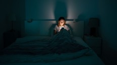 Woman in the dark scrolling through her phone. Woman lying in bed scrolling on phone.