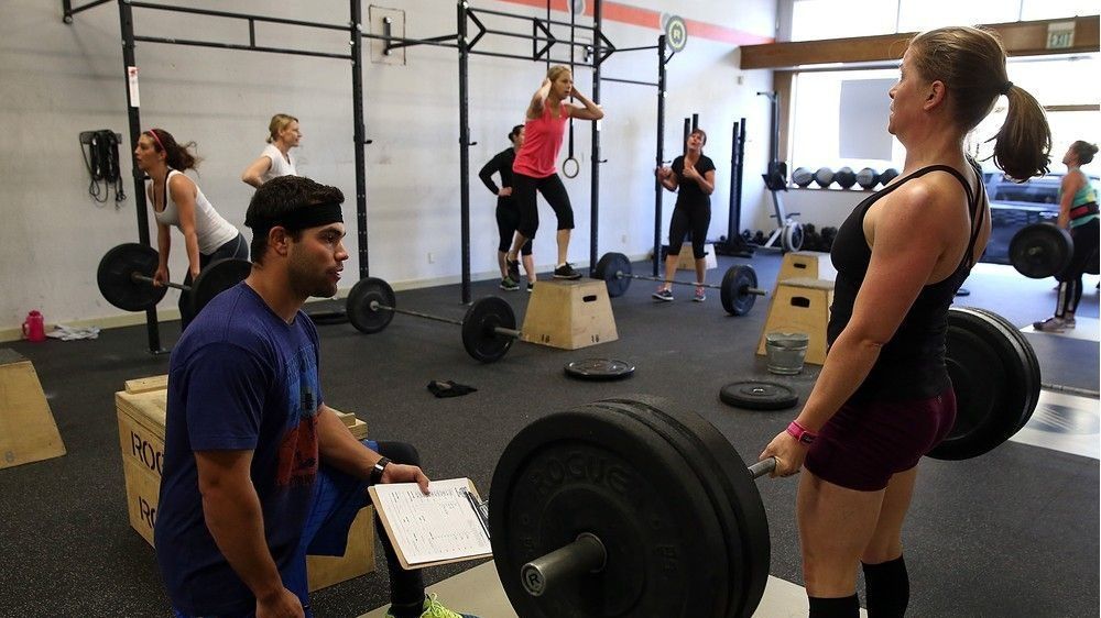 trainer watching student lift weights in the gym. male trainer coaching female student while working out.