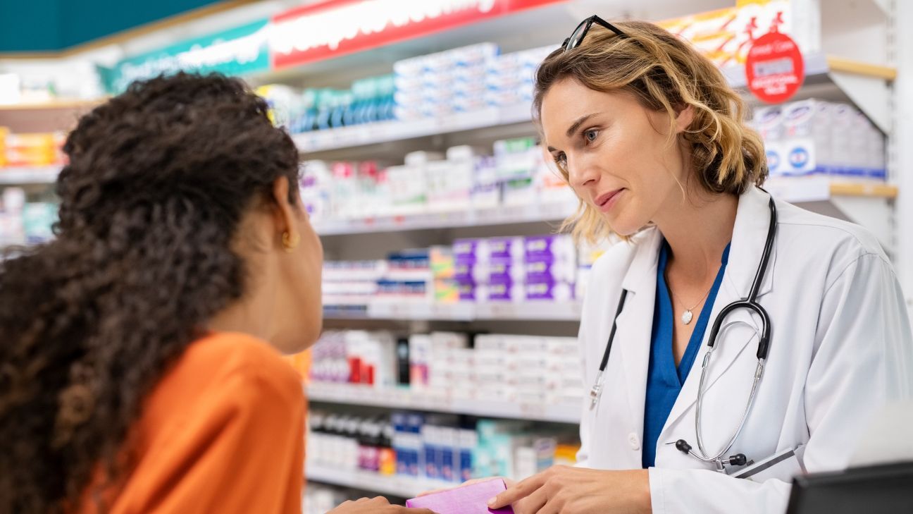 Pharmacist giving medicine box to customer in pharmacy. Doctor showing and explaining medicine dose to customer.