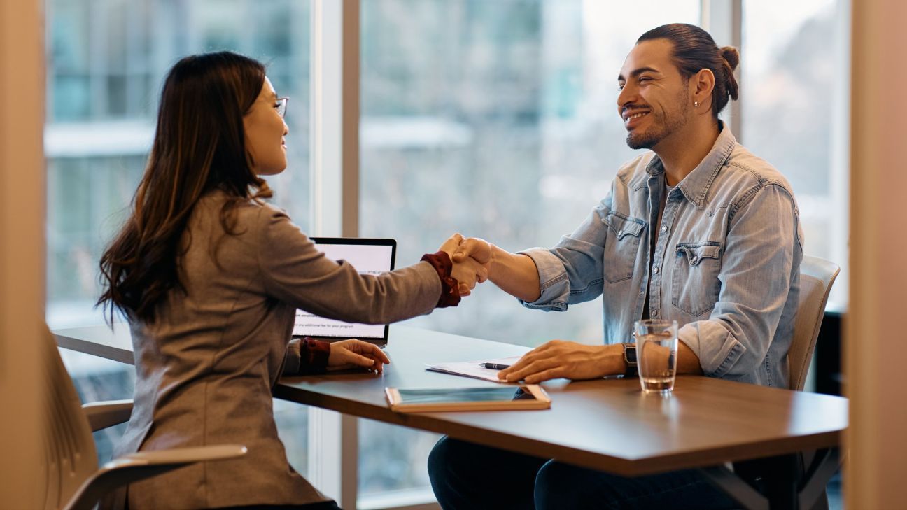 Human resource manager shaking hands with male candidate during job interview in the office