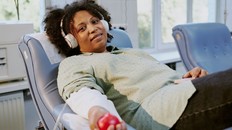 Woman relaxing on donation chair, holding red ball and wearing headphones, during blood donation process in bright medical room