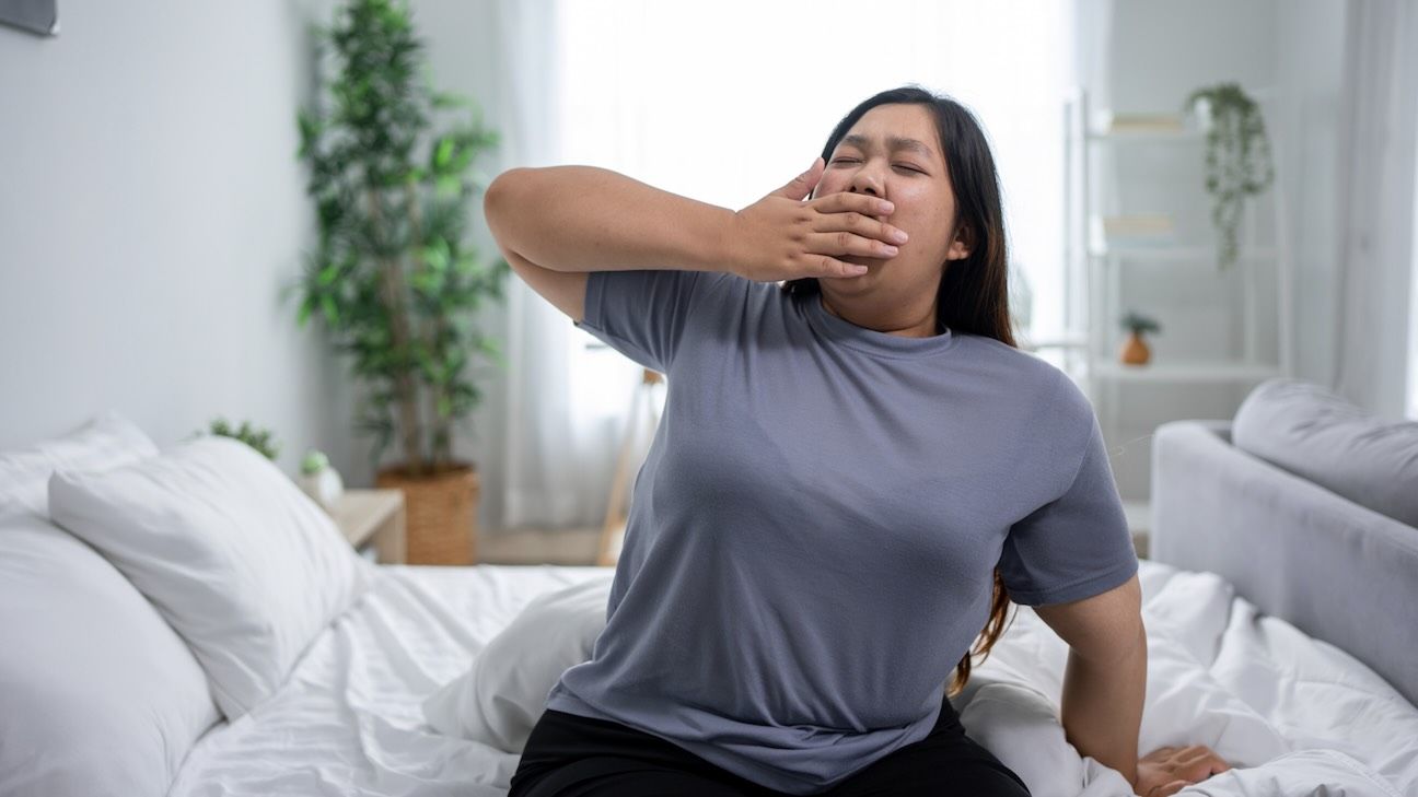 Woman sitting on bed yawning and stretching.