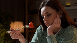 young woman looking at food on a fork. bored and disinterested woman looking at food.
