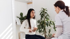 Woman talking to her doctor while holding her abdomen in discomfort.