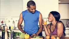 Man and woman laughing together in the kitchen while making healthy food. Both people wearing fitness clothing.