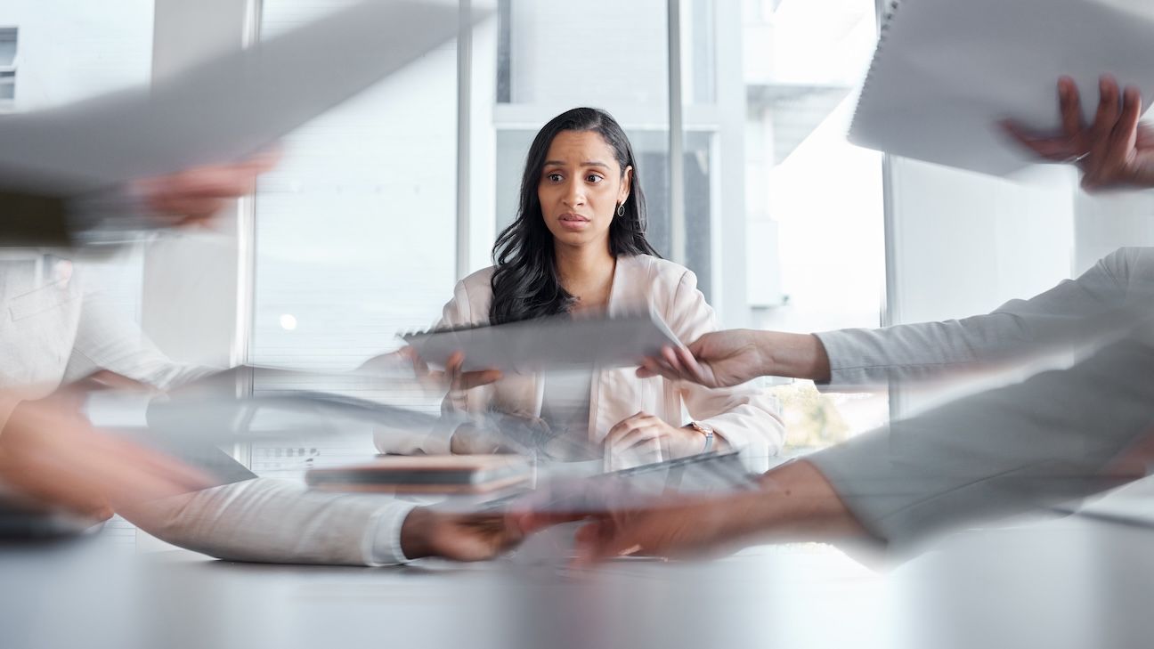 Woman sitting in business meeting experience social anxiety. Papers being passed back and forth by concerned woman.