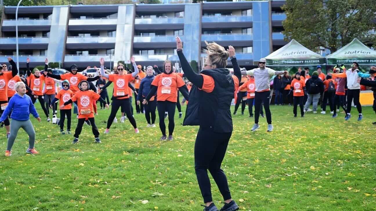 A woman, Alethea Greyeyes stands in front of a crowd of runners wearing orange shirts for National Day for Truth and Reconciliation hyping them up for a charity run.