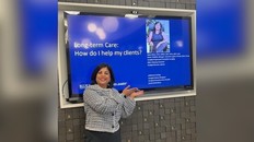 Neela White, woman posing for a photo next to a presentation on a tv screen.