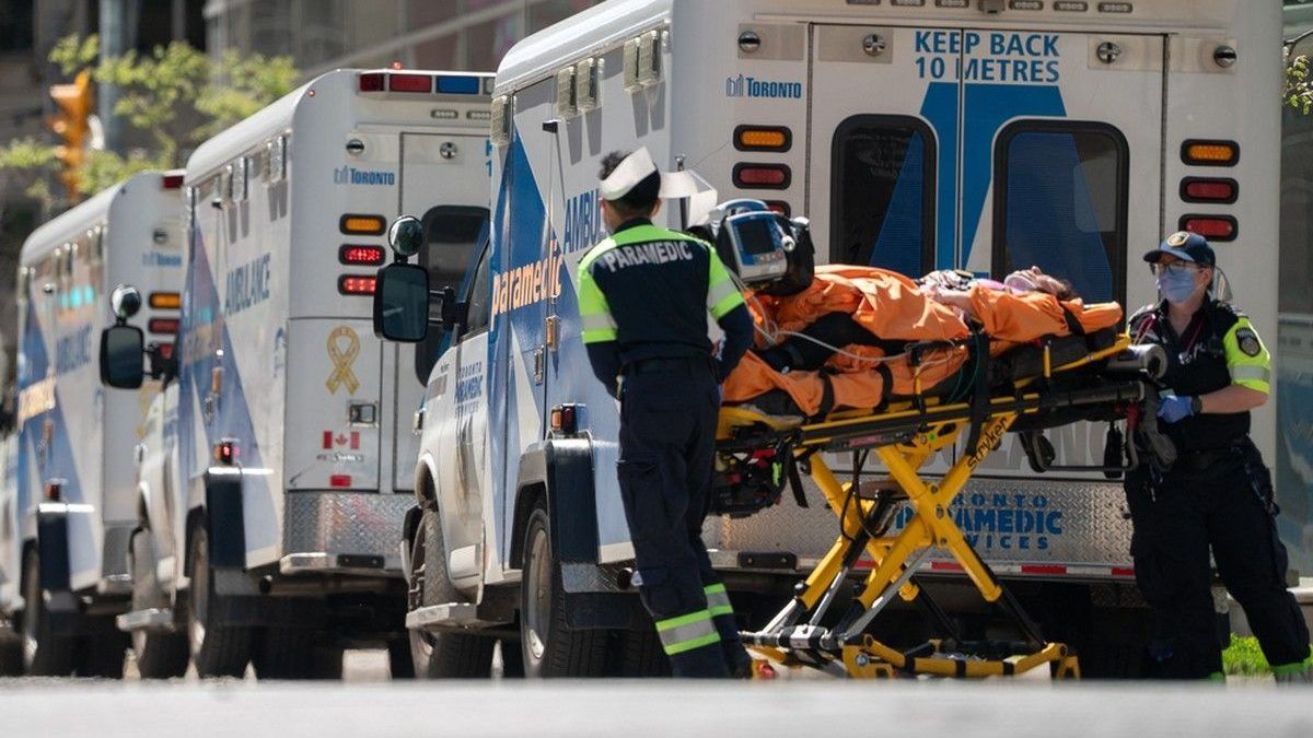Ambulances and paramedics pushing hospital beds around the outside of an emergency department.