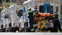 ambulances and paramedics pushing hospital beds around the outside of an emergency department.