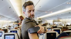 A man stands in a plane aisle checking his blood sugar levels using a continuous glucose monitor and smartphone.