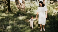 A women, Yvonne Li, smiles down at her son while they walk hand in hand through a beautiful, lush forested area.