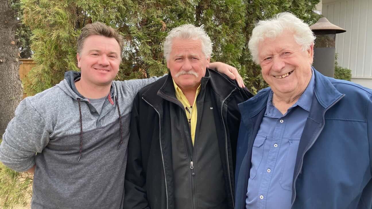Three men standing together smiling for a photo with trees behind them