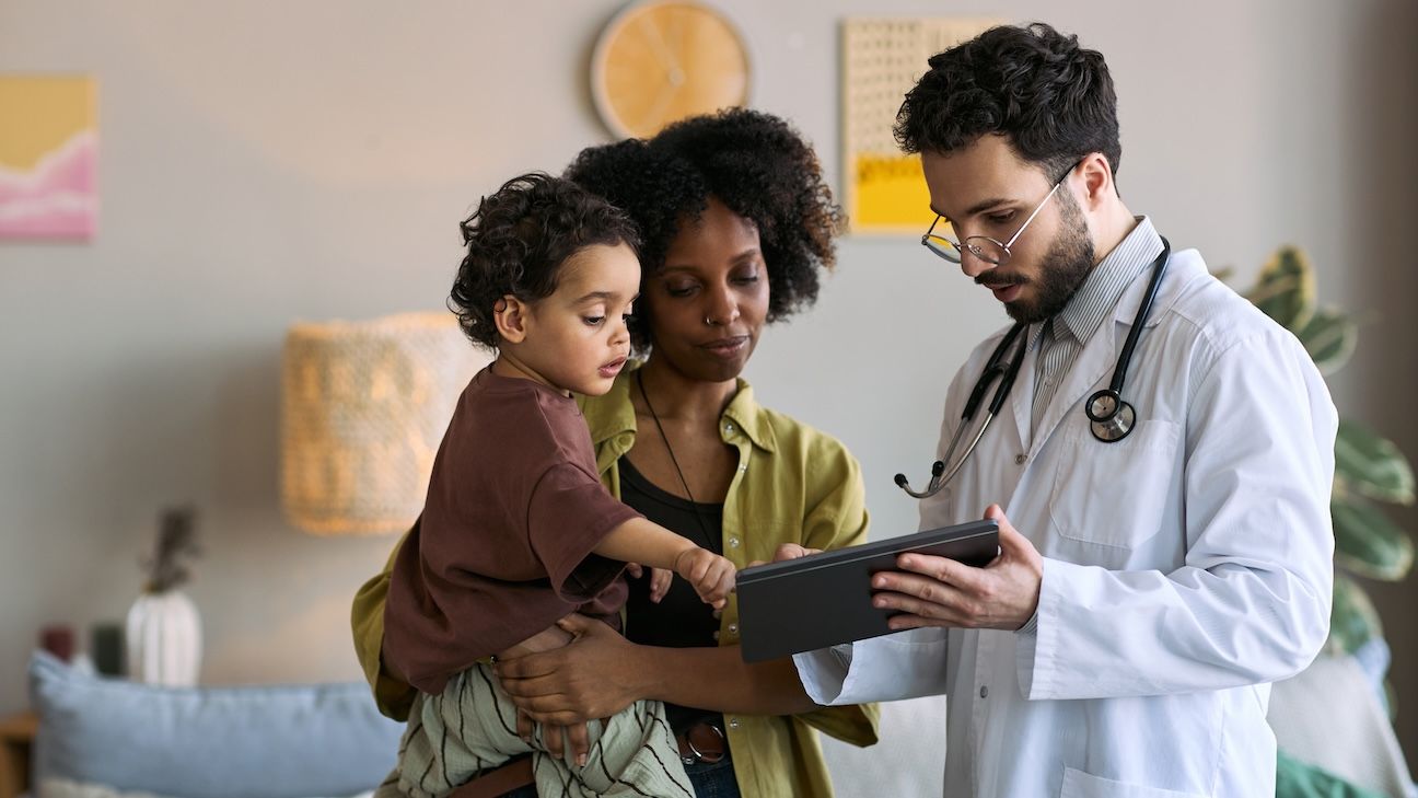 African American mother holding child while doctor showing tablet during home visit, discussing pediatric care and treatment