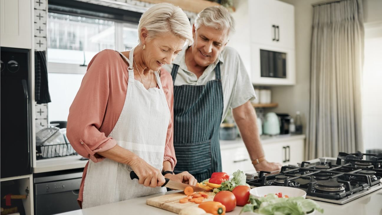 Senior couple, healthy food and cooking lunch together in Australia kitchen at home. Happy woman, hungry man and retirement people cut vegetables for nutrition diet, wellness and vegan dinner meal