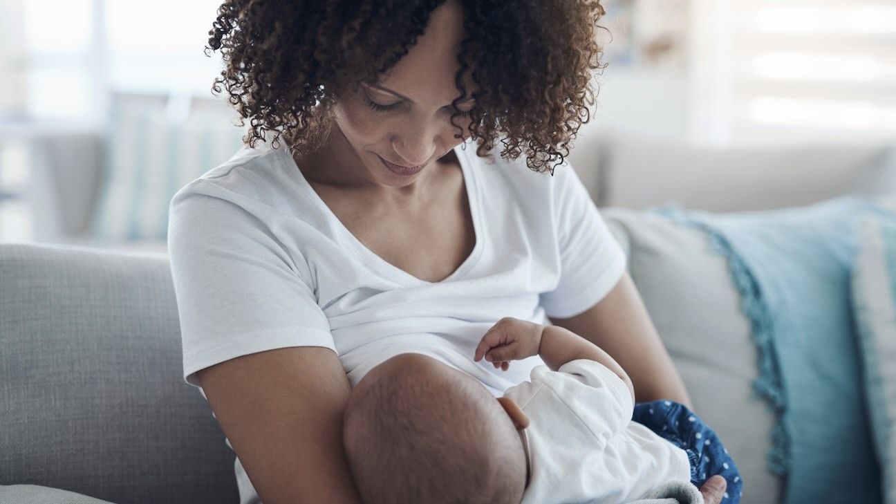 Love, living room and mother breastfeeding her baby for health, nutrition and wellness at home. Bonding, care and young woman nursing or feeding her newborn child milk on the sofa in the family house