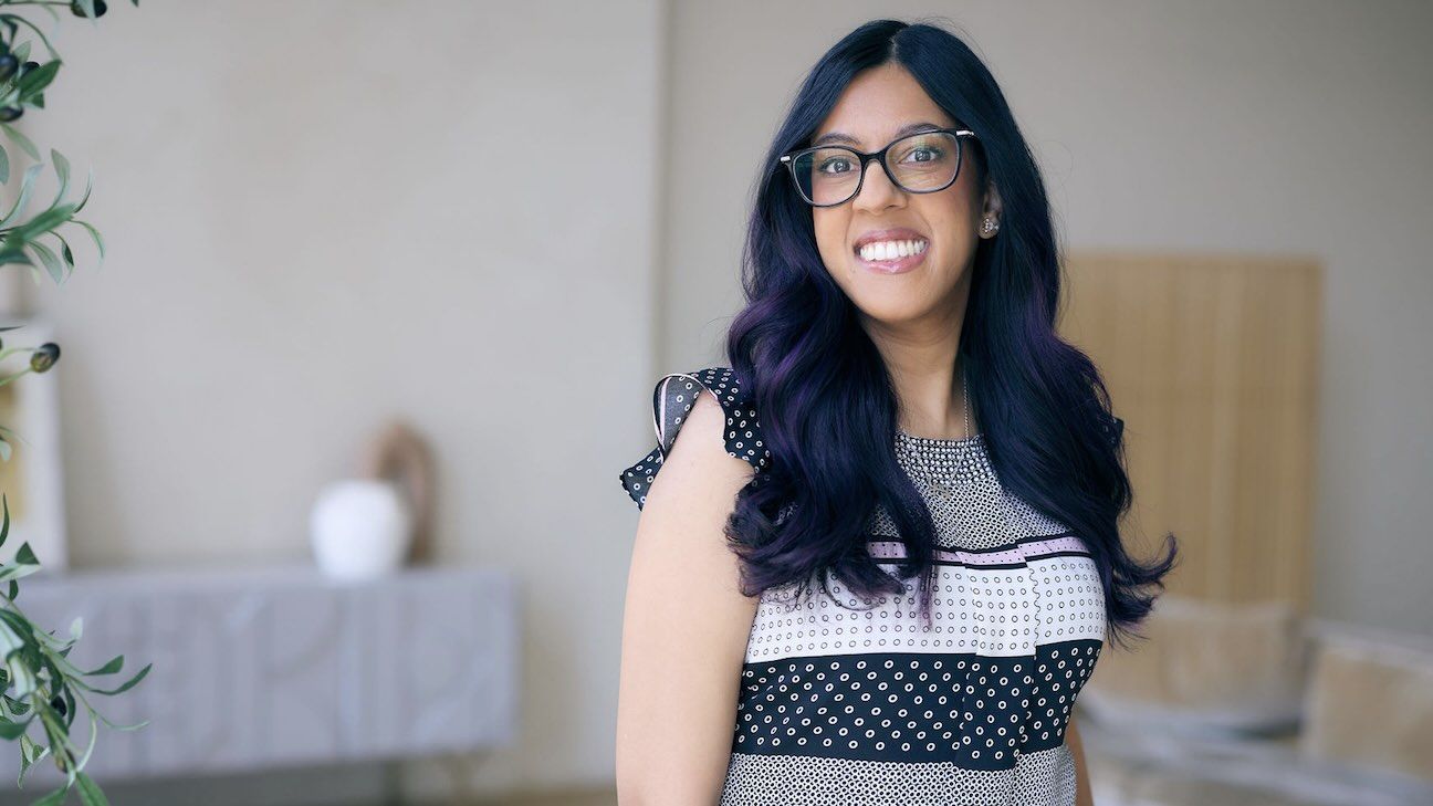 A women stands in a mininalistic room smiling and posing for the camera.