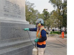 Bill Ross (left) and David Stallard of RMW Industrial Services work cleaning the Cenotaph in Victoria Park after it was vandalized overnight in Regina.