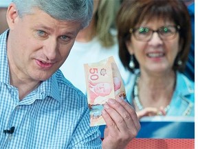 Conservative leader Stephen Harper holds up a pile of money as he illustrates proposed Liberal tax hikes during a campaign event in Trois-Rivieres, Que., Thursday, Oct. 15, 2015. Canadians will go to the polls in the Federal election Oct. 19.